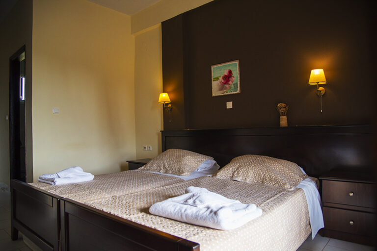 Twin beds with wooden headboard and bedside reading lamps at Villa Maria Perivoli